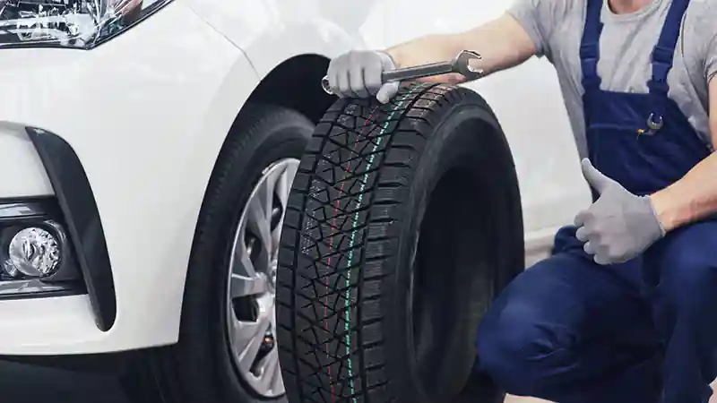 man holding a tire near a white car