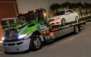 A flatbed of Alfredo Towing Services hauling a White C300 Mercedes Benz.